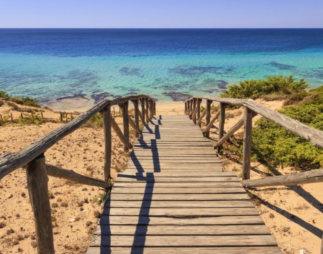 Wooden walkway leading to a beach with crystal-clear water and golden sand.