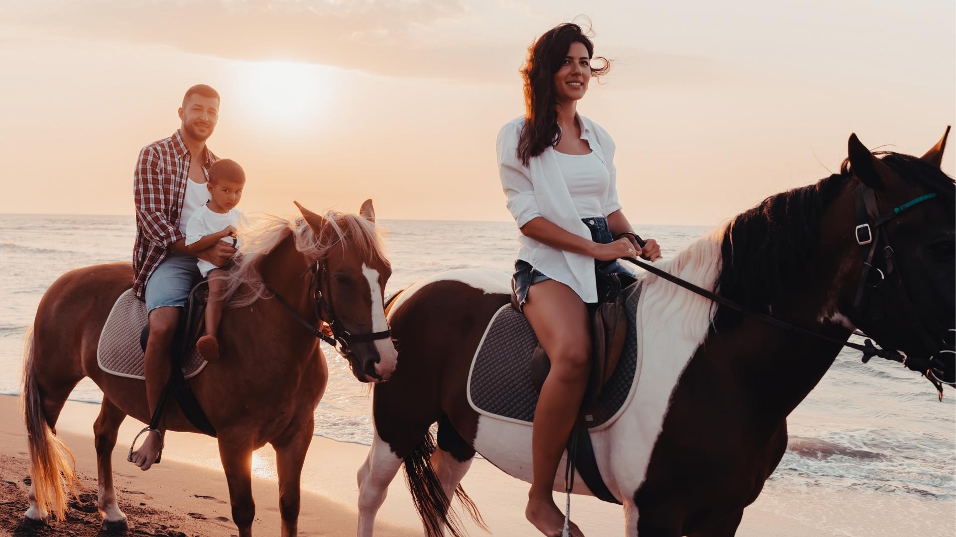 Famiglia a cavallo sulla spiaggia al tramonto.