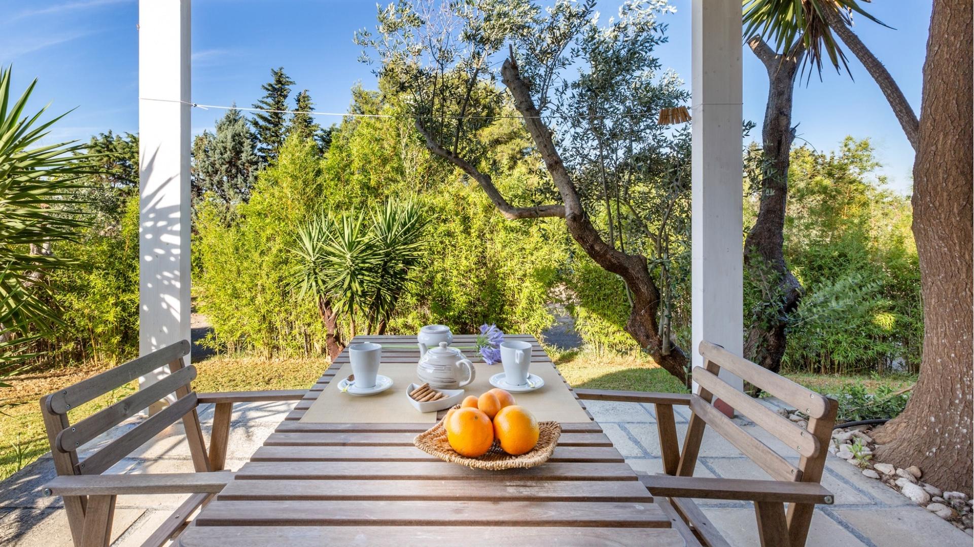 Terrazza con tavolo apparecchiato, circondata da alberi e piante verdi.