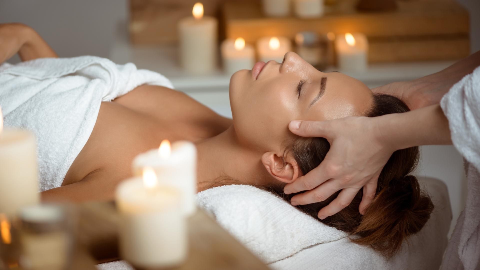 Relaxed woman receiving a massage with lit candles in the background.