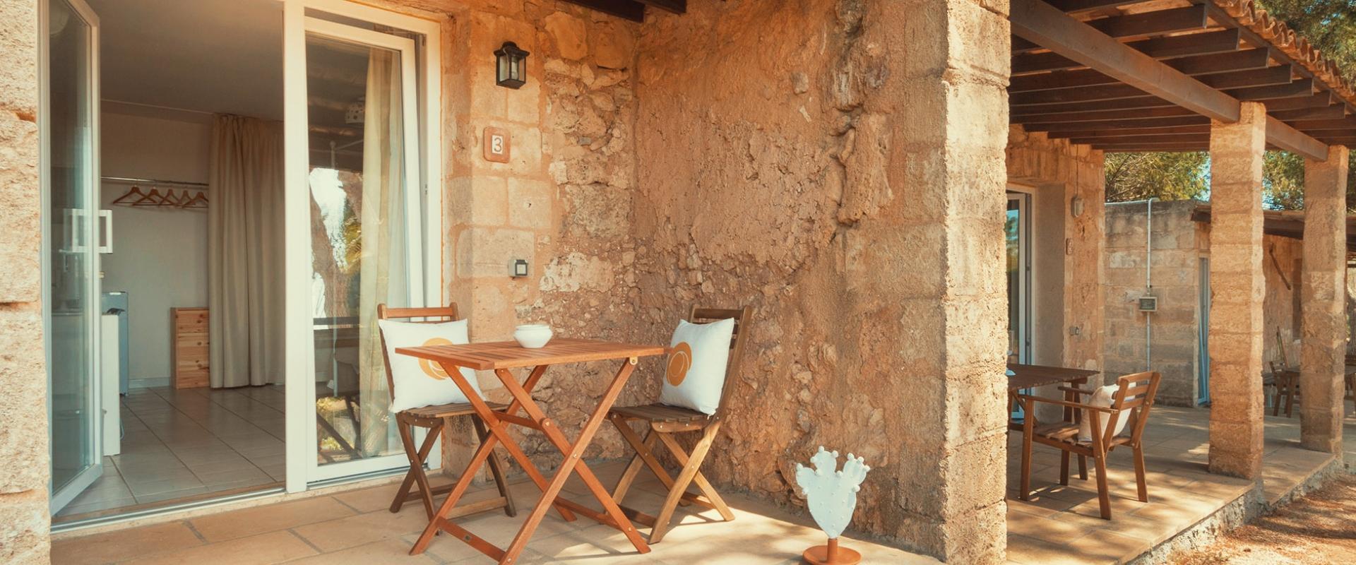 Terrazza con tavolo e sedie di legno, ingresso alla camera con porta scorrevole.