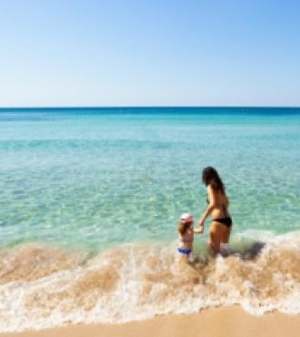 Donna e bambino giocano nelle onde su una spiaggia soleggiata.