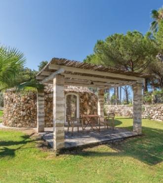 Piccola struttura in pietra con pergola in giardino verde.