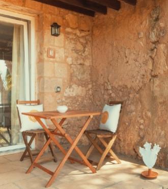 Terrazza rustica con tavolo e sedie in legno, cuscini bianchi e decorazione.