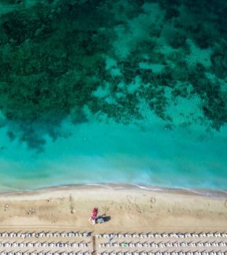 Spiaggia con ombrelloni, mare cristallino e fondale verde visto dall'alto.