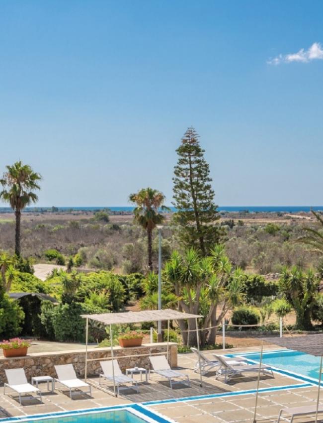 Pool with loungers, sea view, and palm trees in a sunny setting.