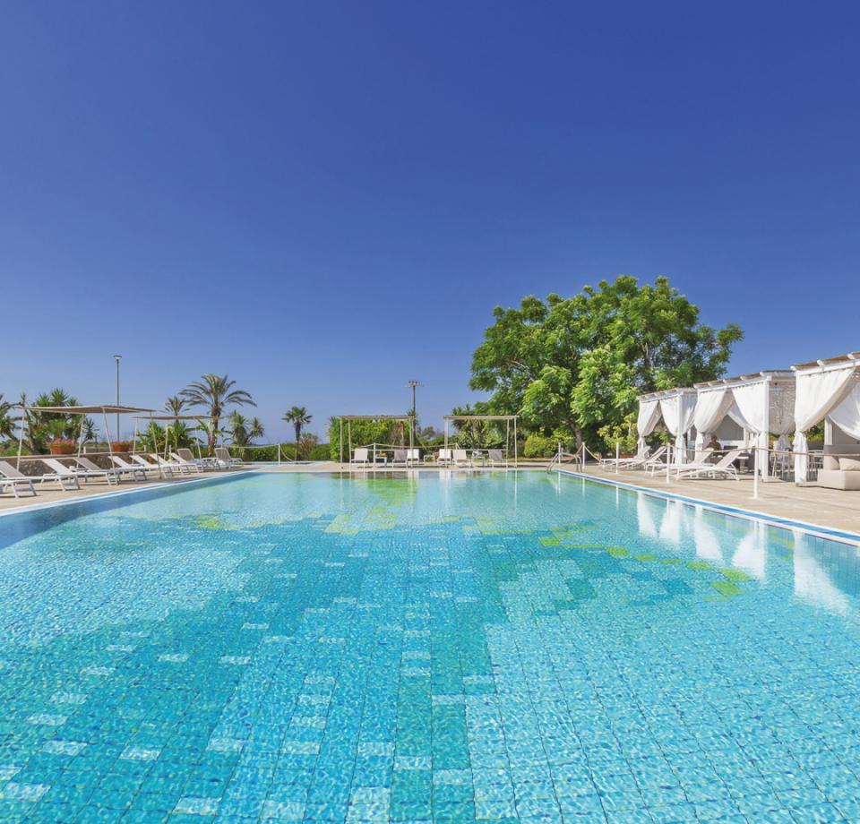 Pool with loungers and white canopies, surrounded by palm trees and greenery.