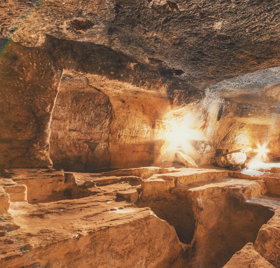 Antica grotta di pietra con scale illuminate dalla luce naturale.