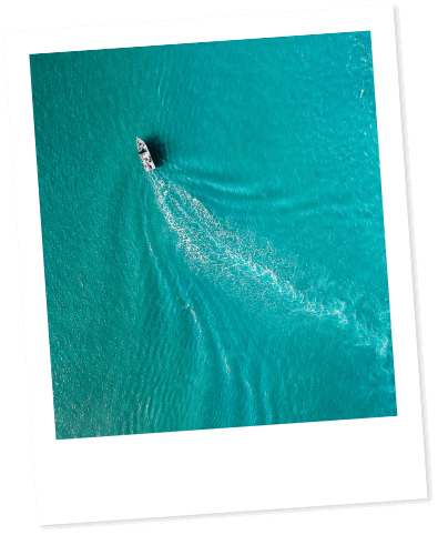 Lone boat sails in turquoise sea, leaving a white trail.