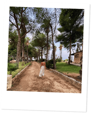 Woman walking on a tree-lined path on a serene day.